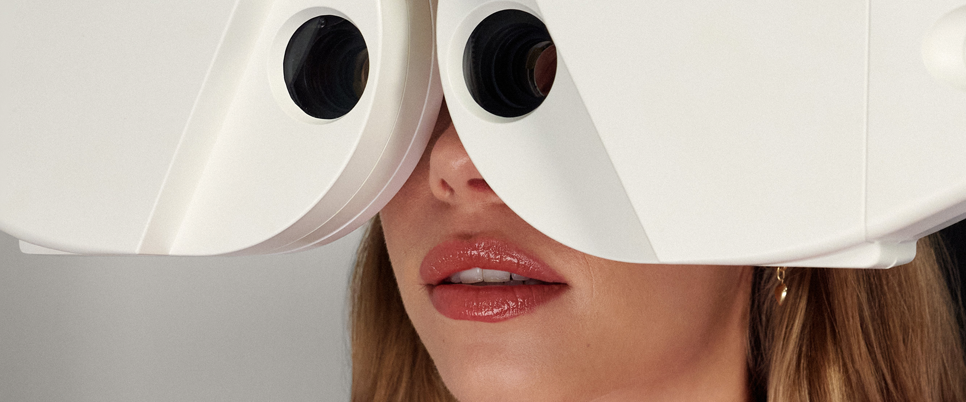 Close-up of a woman looking into a white optical examination machine.