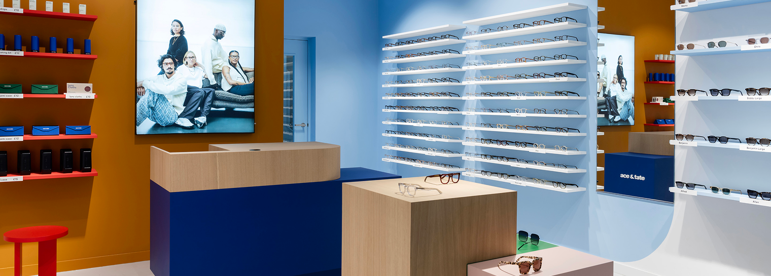A visually striking Ace & Tate retail location with blue and white walls and illuminated wall displays of various eyeglasses and sunglasses.